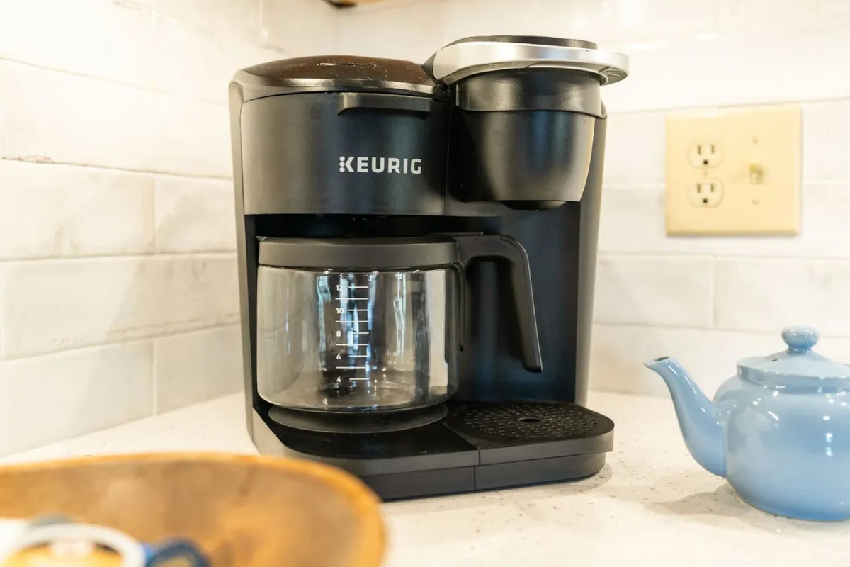 This detail shot features a Keurig coffee maker, a glass coffee pot, and a blue teapot arranged on a counter—conveying the aroma and ritual of enjoying hot beverages together.