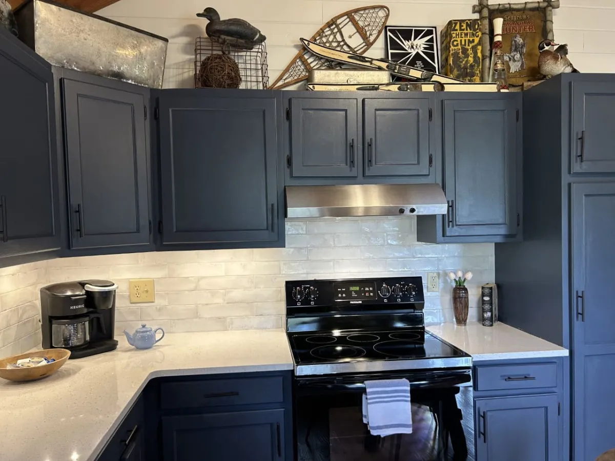 A close-up of the newly renovated kitchen with striking dark blue cabinetry, stainless steel appliances, a white backsplash, and decorative shelving. The modern finishes and spacious layout are perfect for culinary adventures.